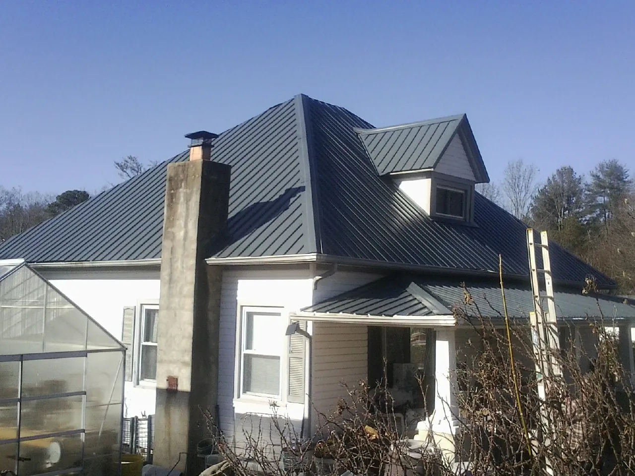 Dark blue standing seam metal roof on a white farmhouse with dormer — Slate & Tile Roof Repair by Roofing Brothers in Chokio