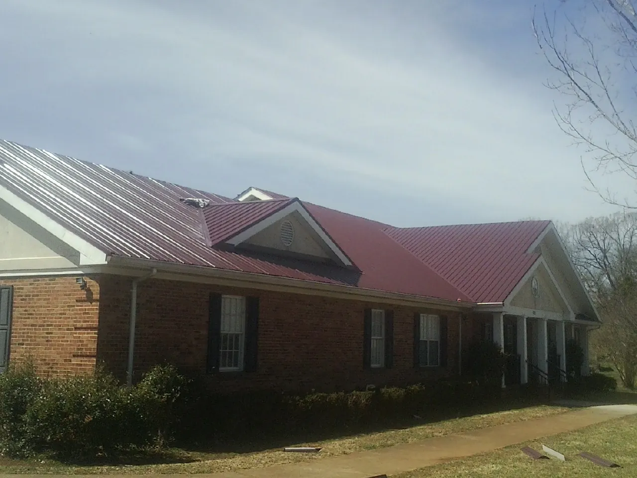 Red metal roof with gabled entries on a long brick building, from a Hail Damage Roof Repair job in Chokio