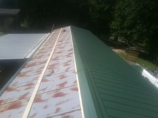 Old rusted panels beside newly installed green metal roofing — Wind Damage Roof Repair by Roofing Brothers in Chokio