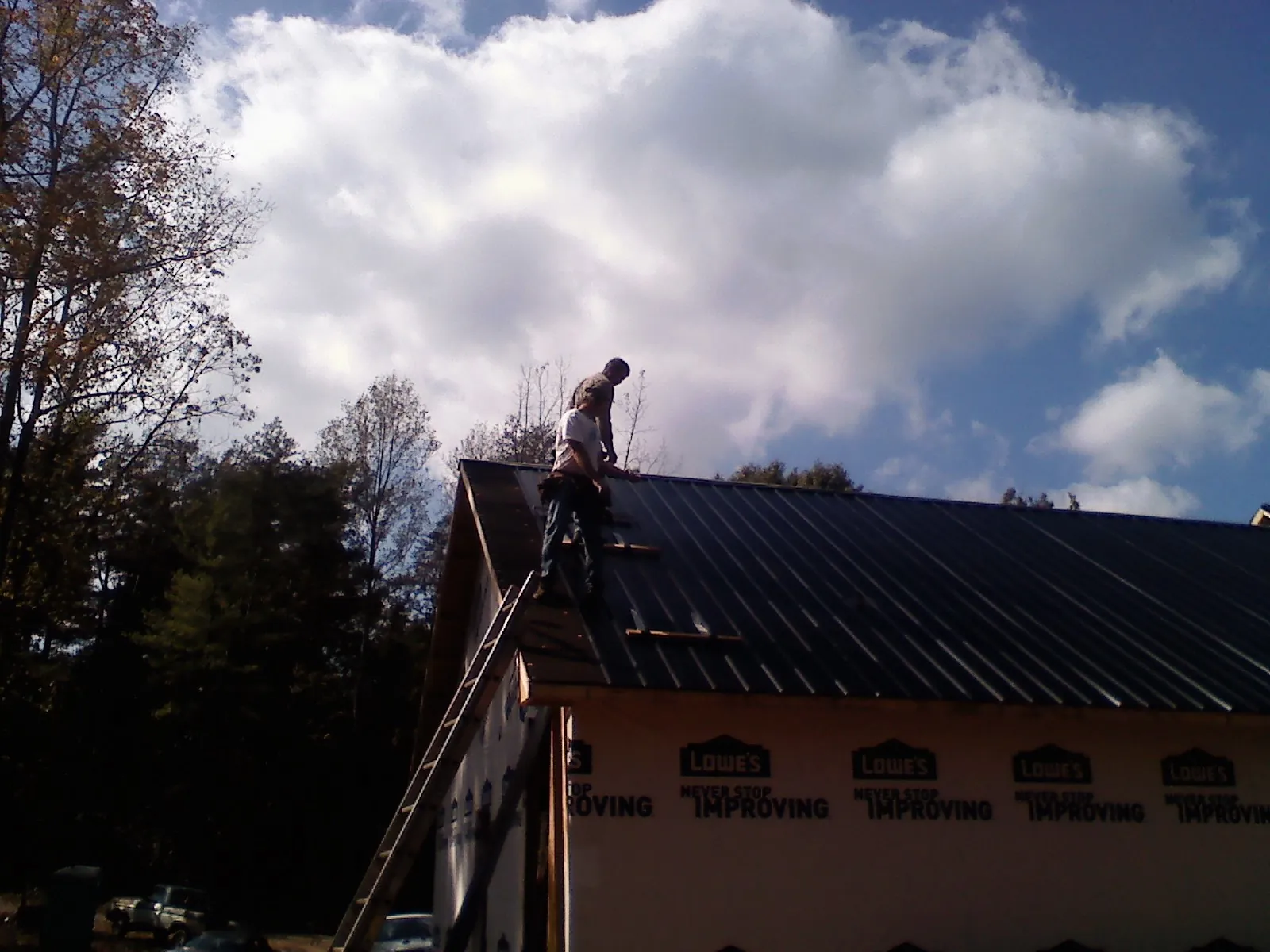 Roofer fastening dark metal panels high against a cloudy sky, from a Roof Inspection job in Chokio
