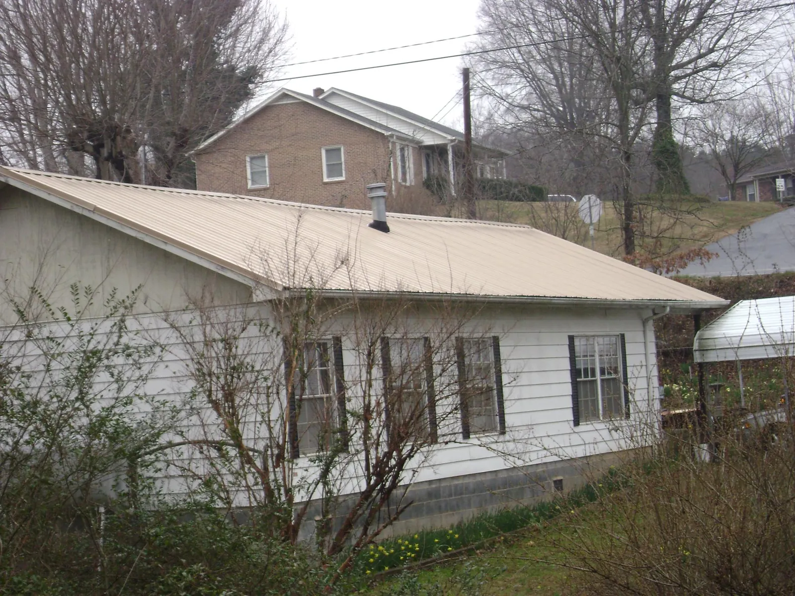 Tan metal roof on a white sided house set into a hillside — Commercial Roofing by Roofing Brothers in Chokio